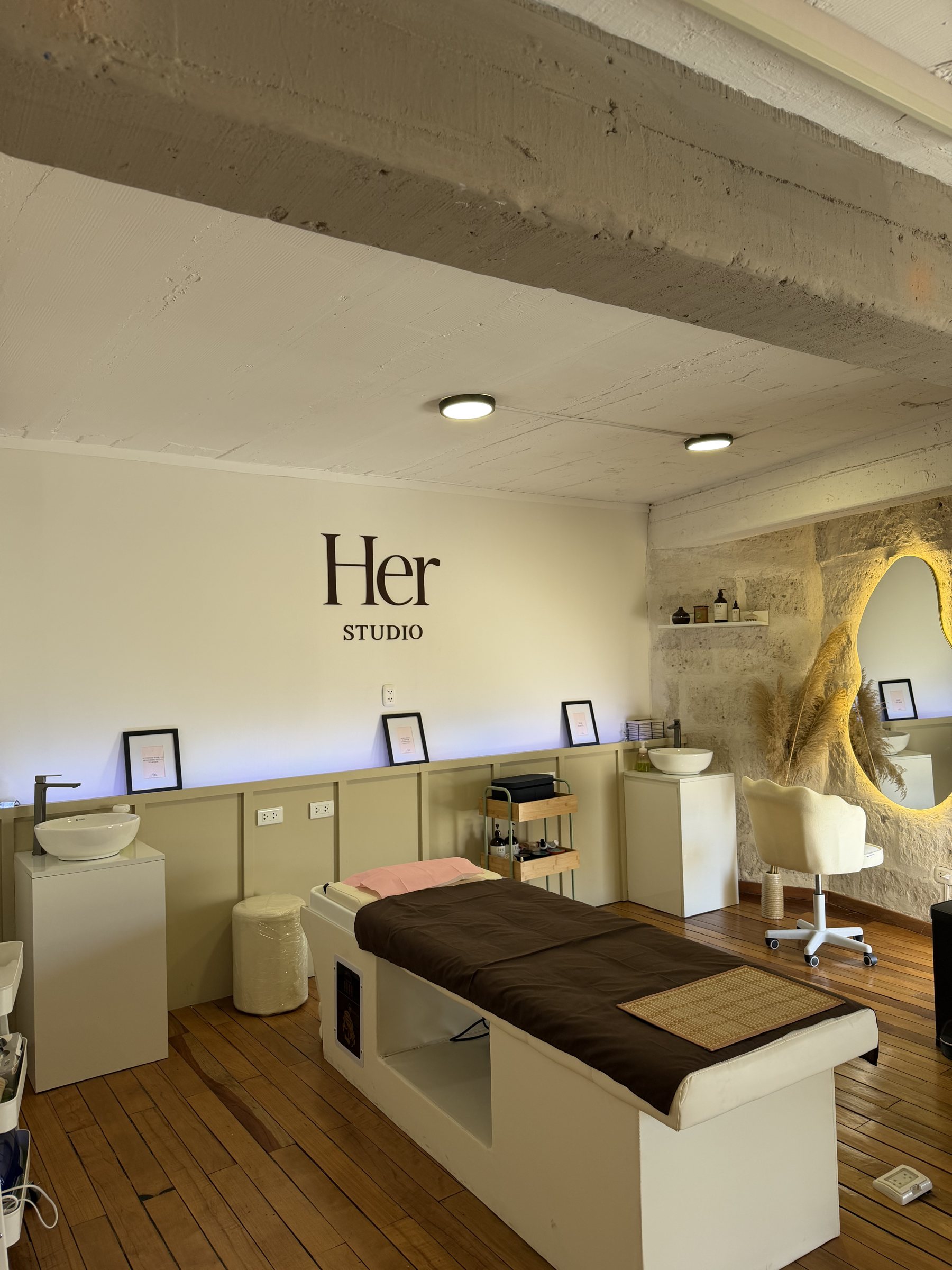 Sala de tratamiento de HerStudio con el logo pintado en la pared, piedra sillar y camillas de cuero