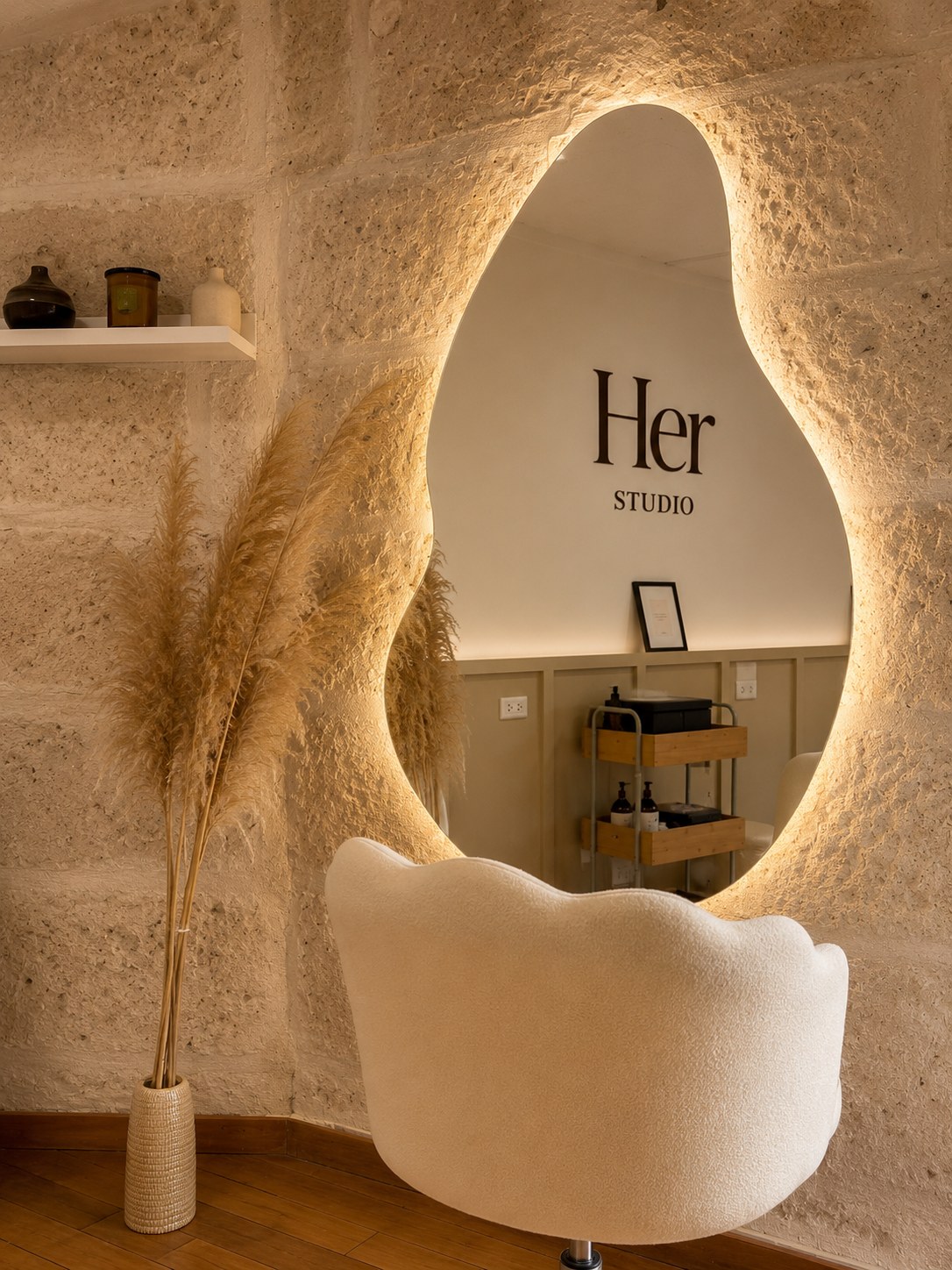 Espejo ovalado con luz cálida en HerStudio, con el logo reflejado en la pared
